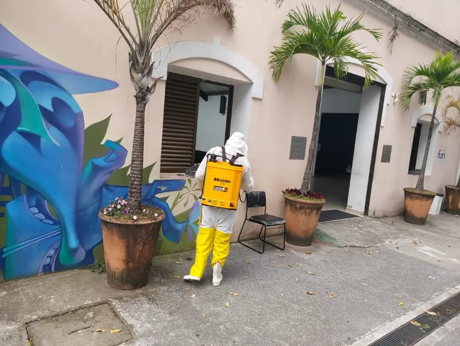 Técnico da Insetivan uniformizado com EPI aplicando sanitização na entrada de um prédio